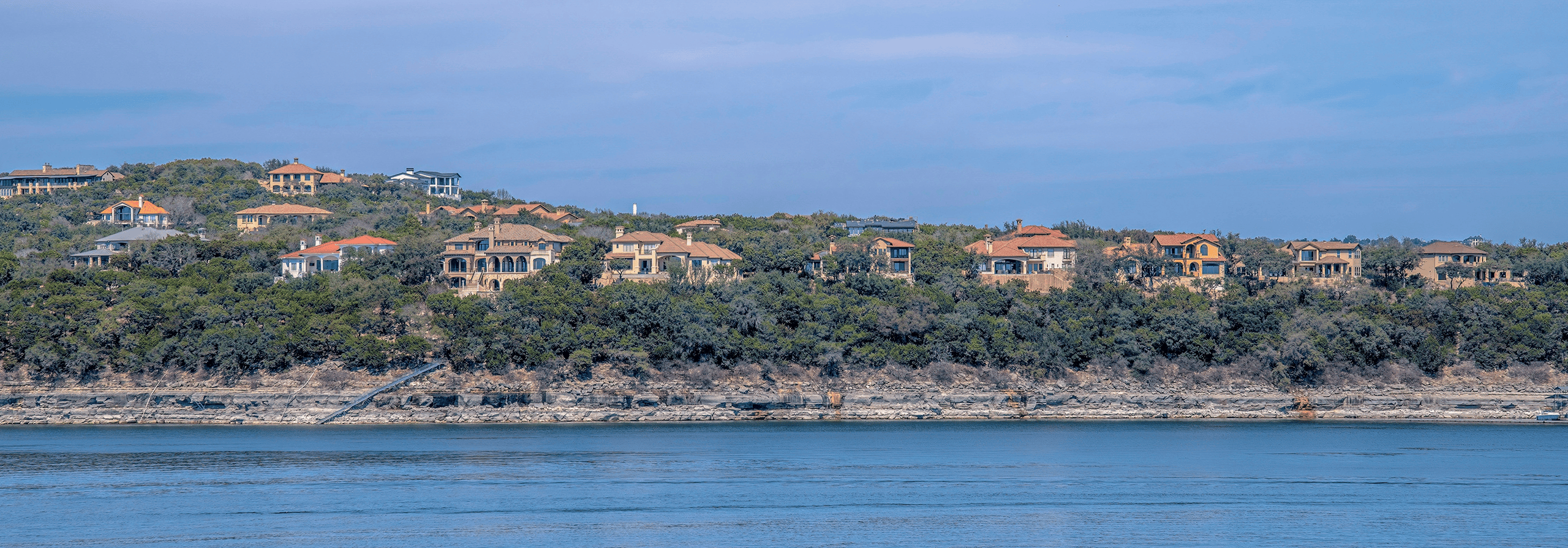 Mansions on a slope with Lake Austin waterfront- Austin, Texas. Rich neighborhood near the lake with mansions and villas on a sloped land against the sky.